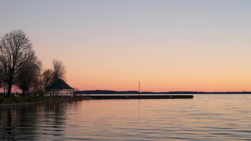 A view of Calm water rippling in a morning scene with a vibrant orange creamsicle coloured sunrise over Lake Couchiching, Orillia, Ontario, Canada
