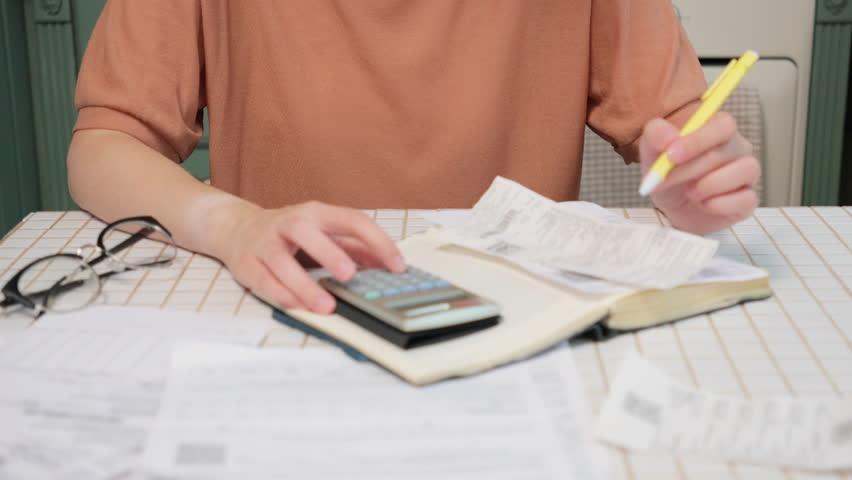 woman pays utility bills in close-up with woman's hand using calculator. Accounting, budgeting and tax calculation, monthly expenses. Female writes expenses in notebook, financial literacy