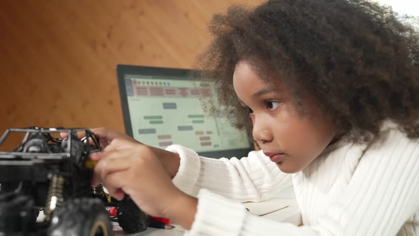 Smart african girl build robotic car while using wires while using laptop setting or writing prompt code. Skilled female student working on computer in STEM technology online classroom. Erudition.