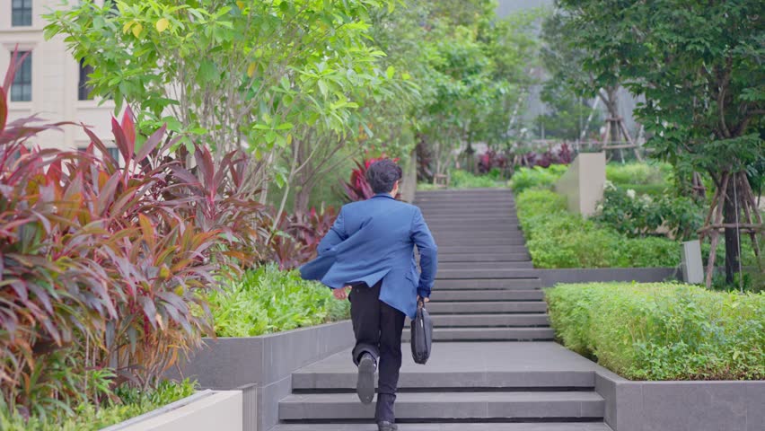 Asian young businessman running up on stairs going to office workplace. Attractive handsome employee man worker in formal suit holding working handbag in hurry walking outdoors in modern urban city.
