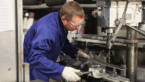 Experienced middle-aged machinist in blue work coat, protective gloves and glasses, focusing on metalworking in industrial workshop, confidently using drill press to create holes in workpiece - Powered by Shutterstock - Get 15% off with code: PIKWIZARD15