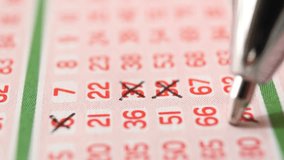 A man marks with a pen numbers 6, 37, 52, 81 on a lottery ticket. The rows of red numbers on the white lottery ticket are arranged vertically. Close-up horizontal video - Powered by Shutterstock - Get 15% off with code: PIKWIZARD15