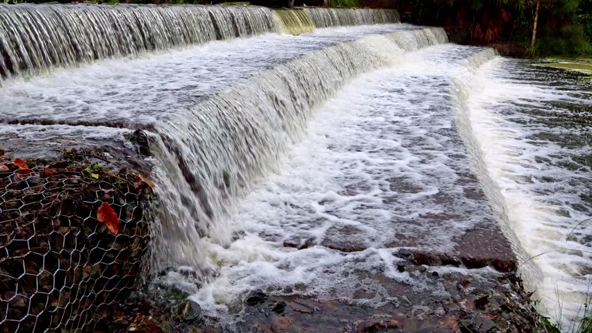 Water flowing and foaming in a flood over one of the stepped weirs which don