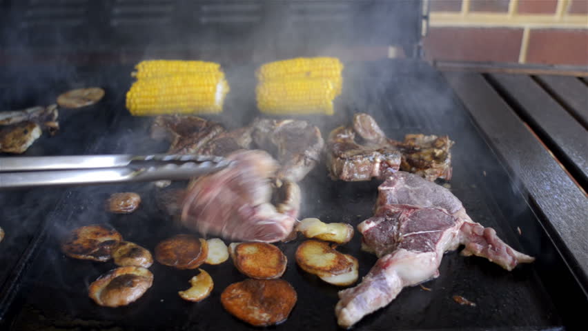 Mutton chops, potato slices and corn cooking on a BBQ hot plate.