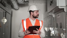 Serious electrical engineer with a beard and hard hat inspects and takes notes on an electrical control panel. Industrial environment of an electrical substation. Close up of a focused man working. - Powered by Shutterstock - Get 15% off with code: PIKWIZARD15
