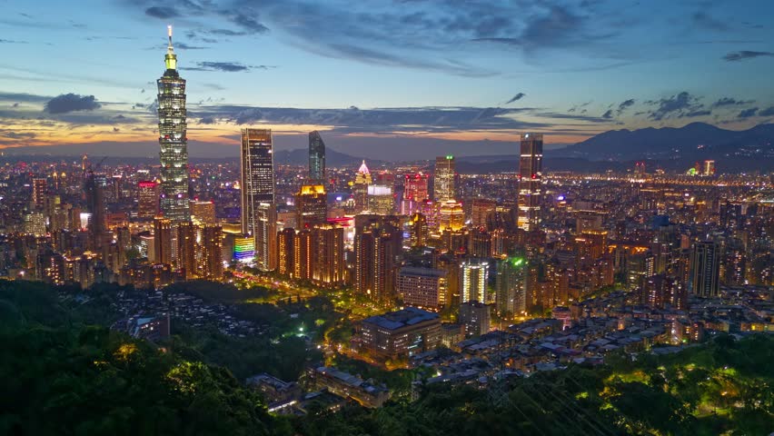 Aerial hyperlapse at sunset above Downtown Taipei, the vibrant capital of Taiwan, with 101 Tower standing out among skyscrapers in XinYi Commercial District and city lights dazzling under twilight sky