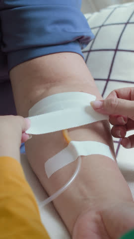 Vertical close-up view of unrecognisable female doctor placing bandage on arm of senior woman during intravenous fluid therapy