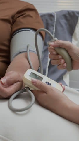 Vertical close-up view of unknown medical worker measuring blood pressure of senior lady with digital sphygmomanometer