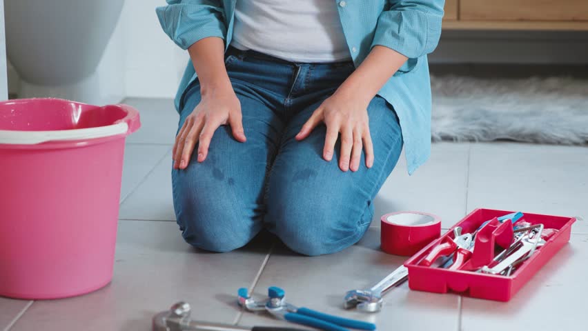 Disappointed woman trying to fix a leaking pipe in the bathroom using some adhesive tape