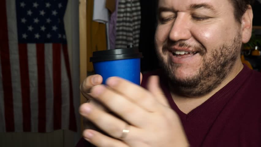 An adult man drinks coffee and talks.