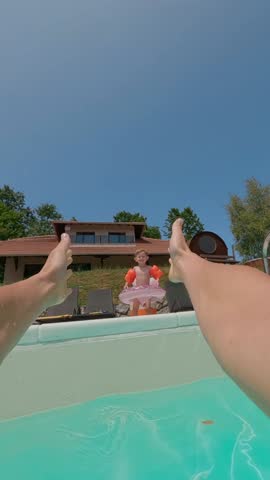 Excited child jumping into a swimming pool, wearing an inflatable ring and floaties, having fun in summer on a sunny day. Slow motion, vertical video