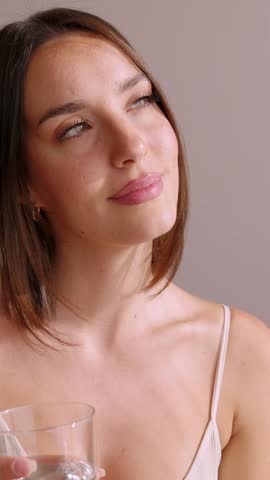 Vertical HD video of young woman drinking glass of mineral water in the morning at home. Healthy lifestyle and well-being concept.