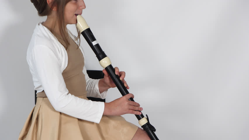 Girl playing, practicing the flute, playing a melody on a musical instrument, wooden pipe, sitting on black chair on white background. Out-of-school children activities, lessons