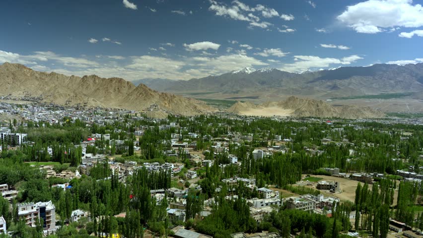 Vibrant Leh city surrounded with green trees and Himalayan mountains under clear blue sky, Leh Palace in view at distance, Ladakh, Kashmir, Timelapse