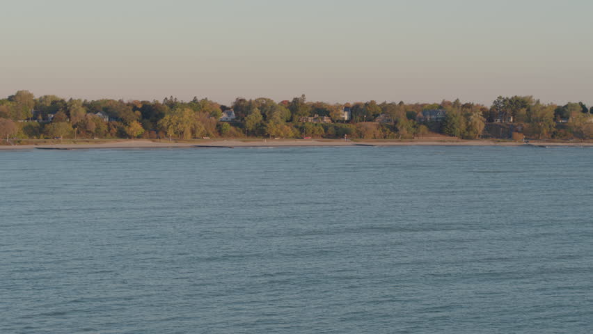 Stunning aerial over peaceful Lake Michigan waves rolling toward the shore and houses in Sheboygan, Wisconsin with vibrant fall colors, serene water, and scenic coastal beauty. Ideal for travel themes