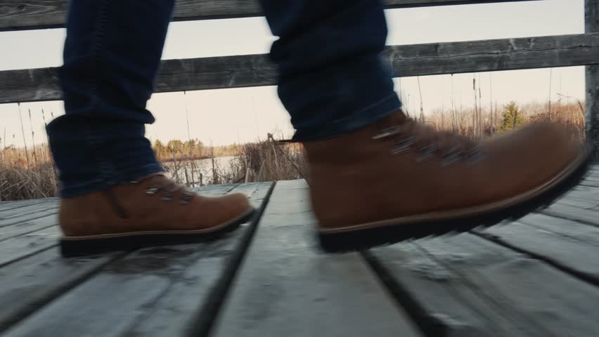 Man In Hiking Boots Walking Across A Wooden Suspension Bridge Over A Majestic Mountain Lake. This Epic Adventure Shows The Beauty And Thrills Of Hiking.