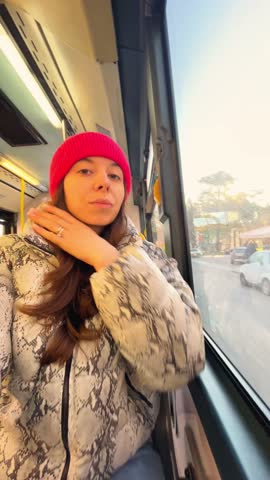 vertical video caucasian brunette girl tourist in bus excursion in red trendy cap and snake print down jacket riding on the bus and looking the window admiring Italian Verona in sunny day