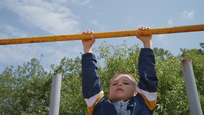 A boy is doing physical exercises on a horizontal bar outside. Strength training for a little boy to grow and be healthy. 