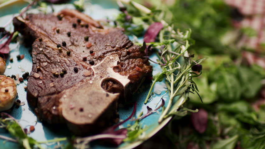Grilled T-Bone Steak Rotating on Table with Fresh Greenery