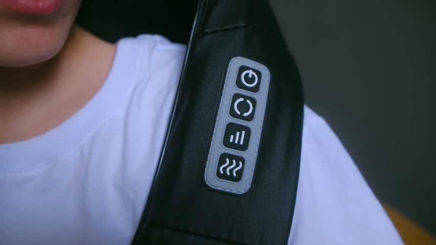 Woman presses Start key on electric massager control panel put on shoulder at home closeup. Female patient enjoys self care with medical equipment