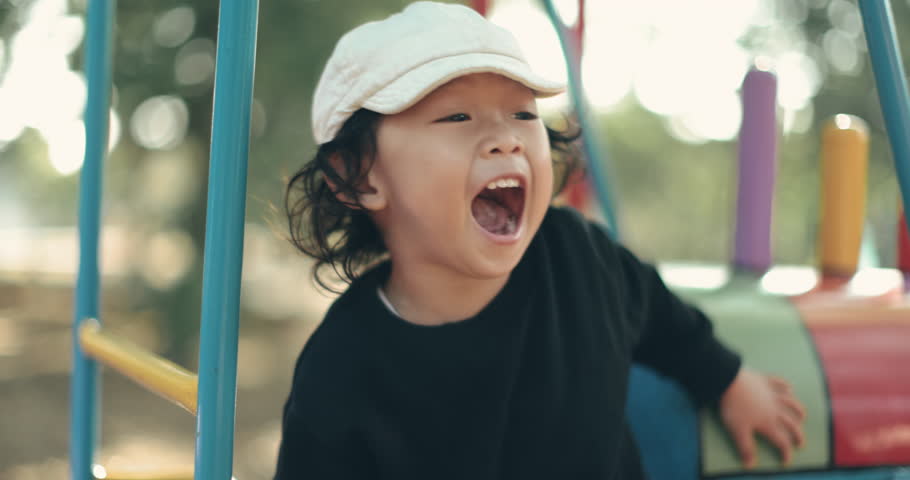 Happy smiling boy playing in playground, wearing a cap and black shirt, enjoying outdoor activity with joyful expression, vibrant background, natural light, and playful mood.4K slow motion.