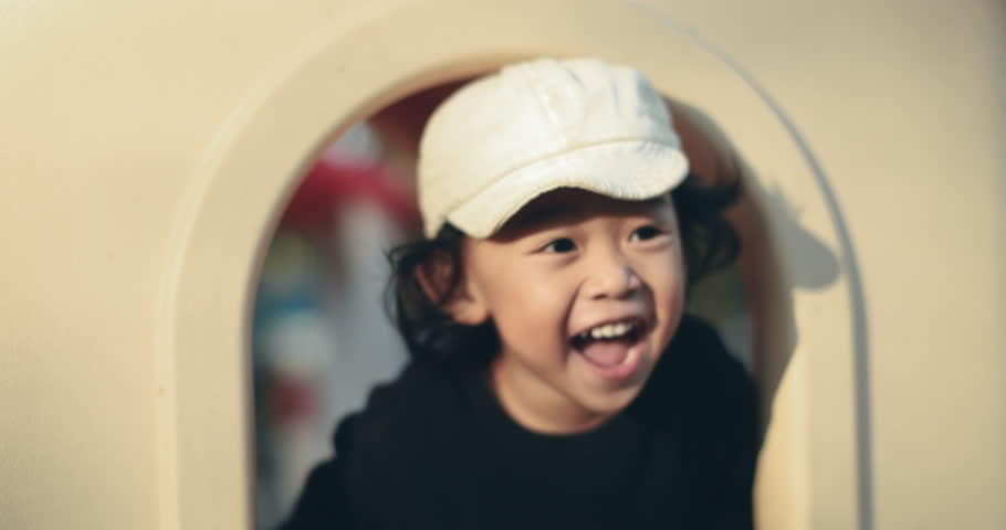 Happy smiling boy playing in playground, wearing a cap and black shirt, enjoying outdoor activity with joyful expression, vibrant background, natural light, and playful mood.4K slow motion.