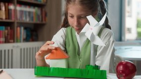 Happy smiling Caucasian little girl child school kid learner pupil student schoolgirl making handmade paper craft house home windmill ecology energy looking at camera showing thumb up indoor classroom - Powered by Shutterstock - Get 15% off with code: PIKWIZARD15