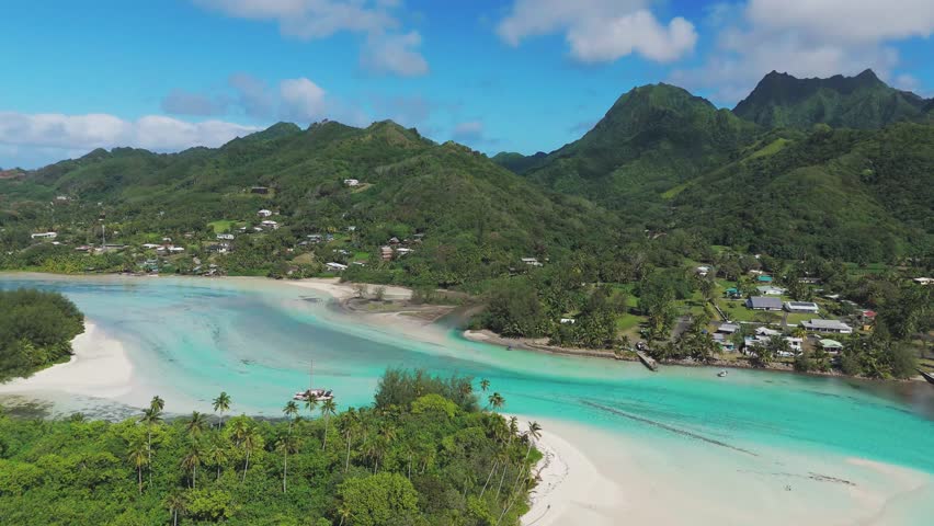 Aerial approaching shot of turquoise water of Muri Beach and Lagoon during sunny day. Coral reef on Rarotonga, Cook Islands. Panorama shot of green tropical mountains in distance. Paradise on earth.