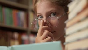 Close up clever smart intelligent Caucasian little girl playful schoolgirl child school kid pupil learner student in glasses eyeglass looking at camera reading book literature inside library education - Powered by Shutterstock - Get 15% off with code: PIKWIZARD15