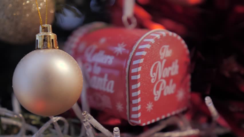 Handheld close-up of a red "Letters to Santa" mailbox ornament surrounded by festive decor.