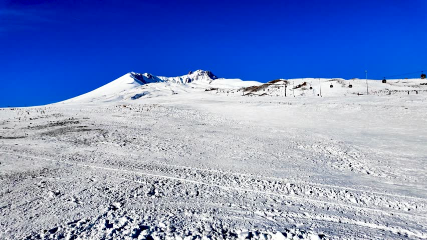 A view of the ski facilities from the Tekir Kapı of the summit of Erciyes, the largest mountain in Turkey. It was taken with a moving camera in the middle of the ski slope. The cable car and people sk