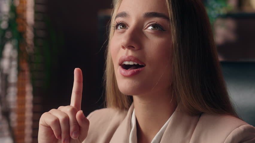 Close up pensive doubtful Caucasian girl employer business woman female businesswoman think remember memory solution having idea raise finger gesture answer insight looking at camera smiling indoors