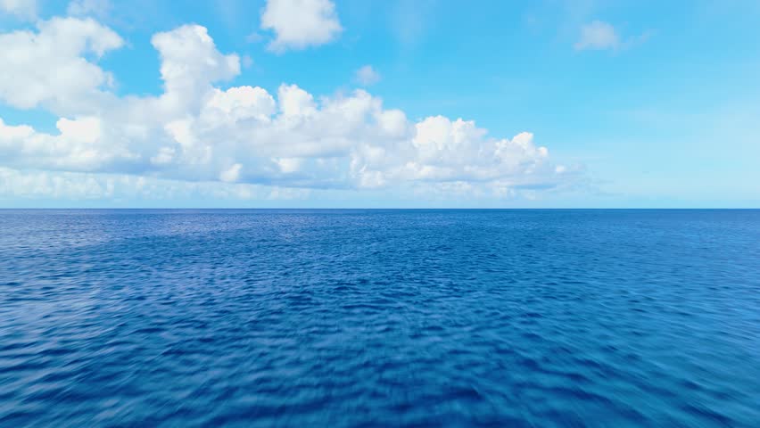 Aerial low fast soaring above clear blue water under a bright sky, calm ocean surface with soft ripples