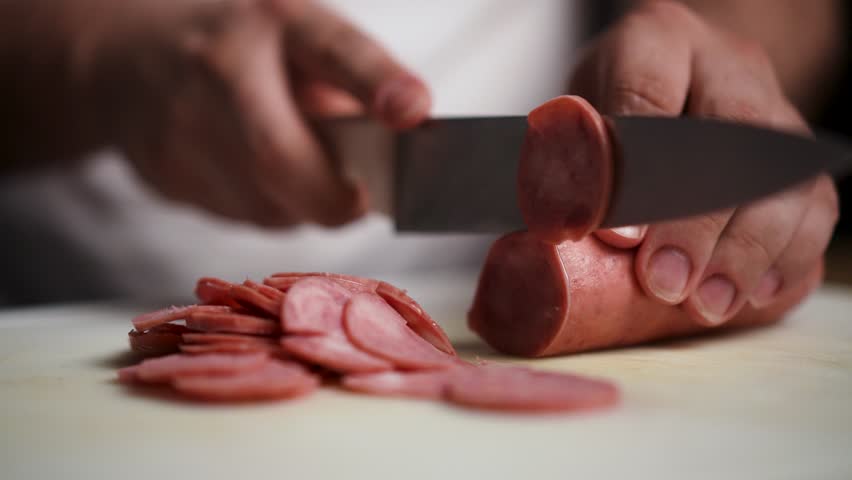 Close-up stock footage of a chef cutting pepperoni into even slices with a sharp knife. Ideal for videos about food preparation, cooking tutorials, or recipes