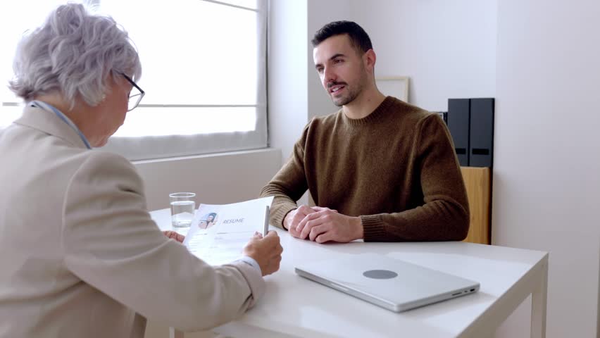Young man doing a job interview with a human resources worker. Job candidate explaining his resume and personal career to senior female recruiter during job interview. 