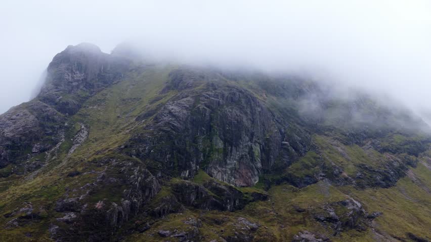 Aerial drone footage of the Glencoe mountain range in the Scottish Highlands, taken in summer on a clear but misty day, morning time.