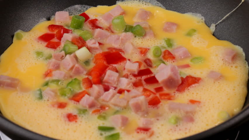 Closeup HD video of an omelette cooking in a frying pan, with hand adding