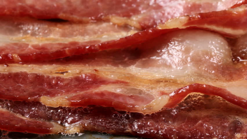 Extreme closeup pan of bacon cooking on a griddle