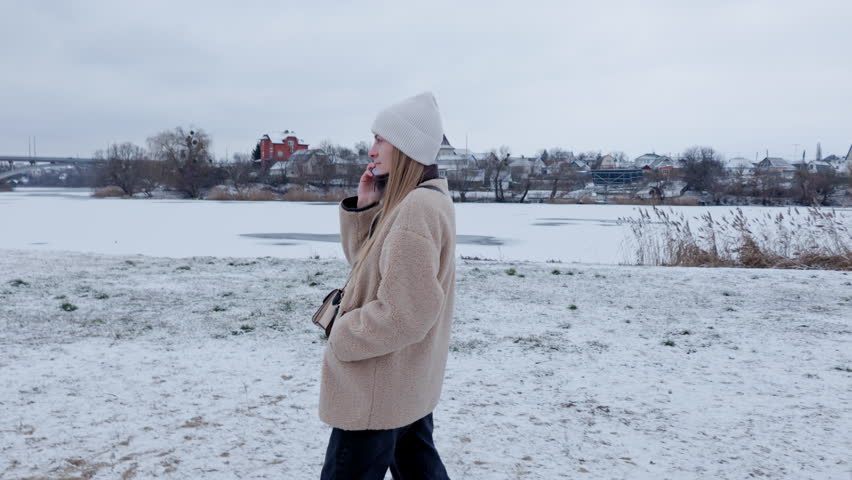 A young woman in winter clothes is talking on the phone outside