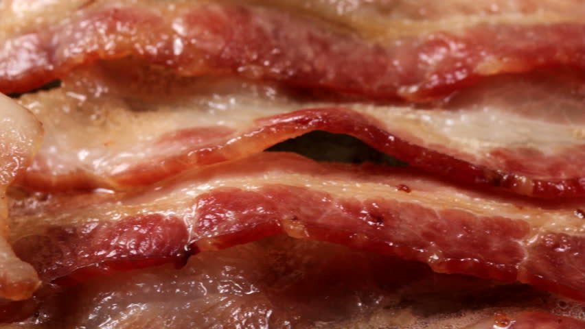 Macro HD video of bacon cooking on griddle. Camera pans from left to right