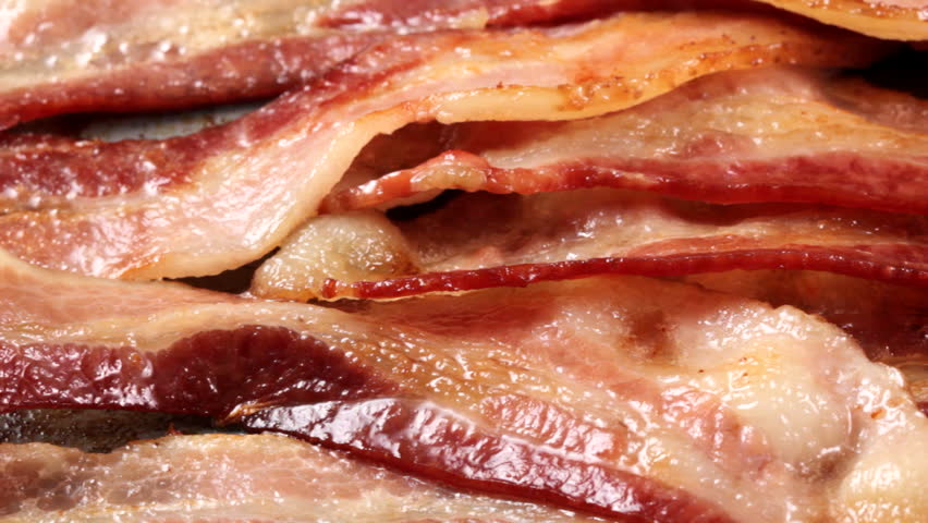 Macro HD video of bacon cooking on griddle, camera pans from left to right