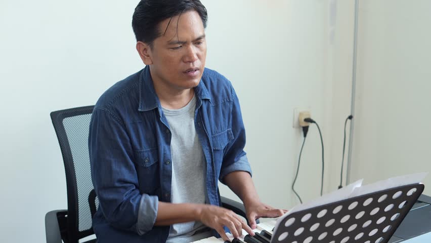 Young Asian Man Enjoy Playing Piano And Singing Song While Looking At Music Sheet At Home Studio