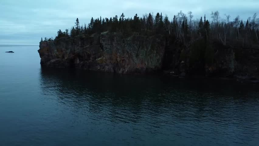 Stunning view of a rugged rocky cliffs wurrounded by forest trees, overlooking a calm lake in Minnesota under a cloudy sky