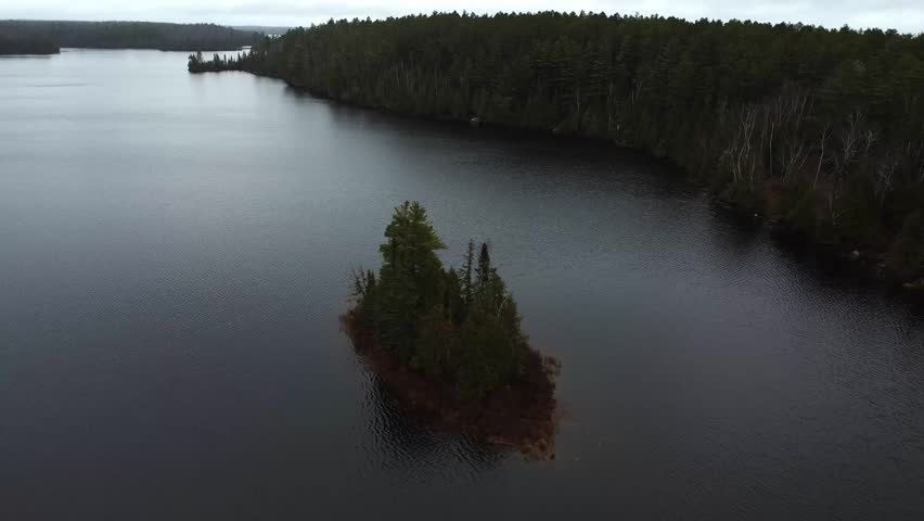 Tranquil View of a small, forested island in the middle of a calm lake, surrounded by peaceful waters in the Boundary Waters, Minnesota.