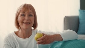 A cheerful elderly woman engages in a fitness session at home. She holds a yellow apple while preparing to exercise with a stability ball nearby, showcasing active living in retirement. - Powered by Shutterstock - Get 15% off with code: PIKWIZARD15