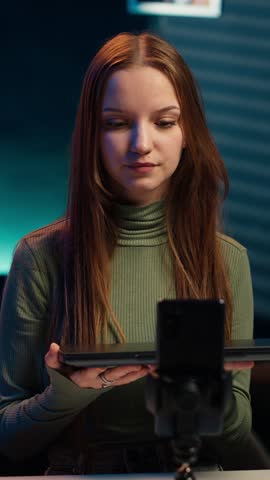 Vertical video Media star fulfilling brand advertising contract by showcasing notebook, filming with smartphone. Teenager presenting followers laptop sponsored by company, recording with phone, camera