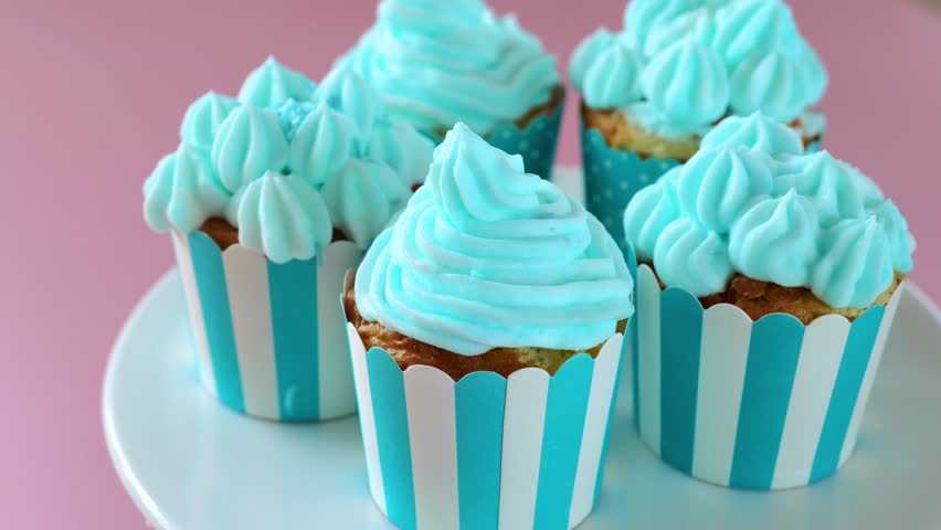 Cupcakes with blue cream. Rotate.Sweet pastries and desserts. Sugar blue decor sprinkles on muffins with blue cream in blue cups on a pink background.candy bar assortment. 4k footage