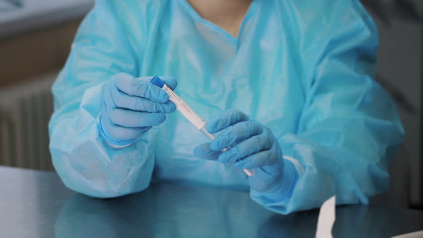 A doctor in a blue protective suit opens the sterile packaging of a swab for analysis. Opening the package with a medical swab. Modern medical laboratory.