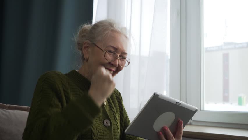 Happy senior woman triumphantly raising her fist after achieving victory in an online game using her tablet