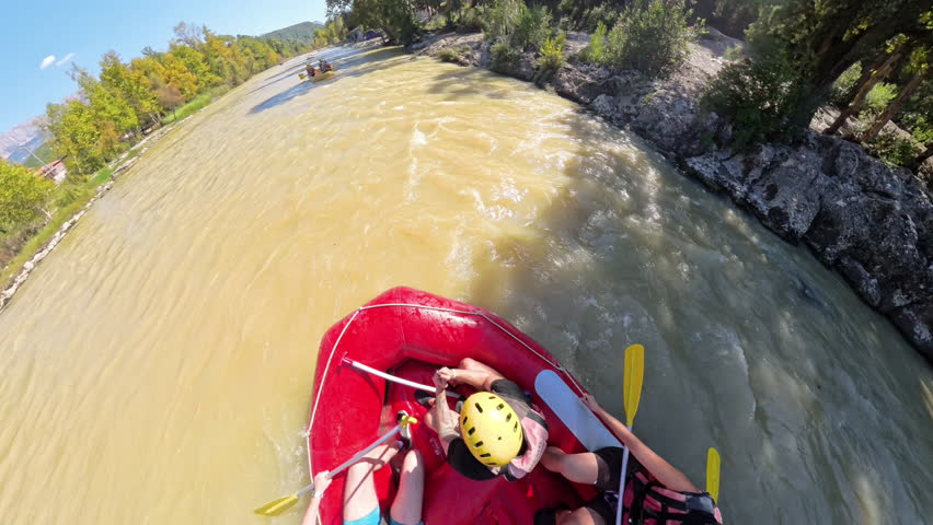 Overhead shot of a group of rafters paddling down a muddy river surrounded by trees, capturing the teamwork and excitement of the rafting experience from a high-angle perspective.